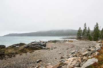 Its a windy, stormy day on the Maine shoreline. This beach is part of the Schoodic peninsula of Acadia National Park. Mist covers the dense pine forest in the background.