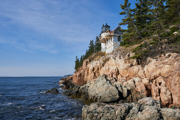 A beautiful clear day with a blue sky at Bar Harbor lighthouse in Acadia National Park. The lighthouse stands above a steep rocky cliff.