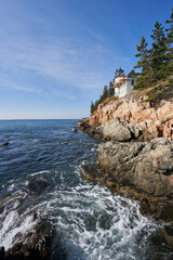 A beautiful clear day with a blue sky at Bar Harbor lighthouse in Acadia National Park. The lighthouse stands above a steep rocky cliff.