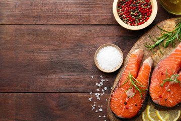 Fresh raw salmon steaks with spices, lemon and rosemary on wooden table, flat lay. Space for text