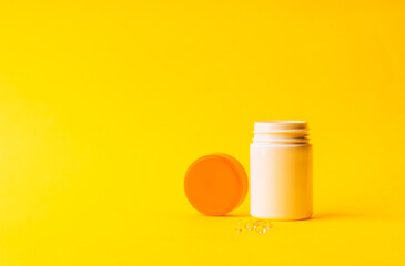 Vitamins soft capsules with pills bottle on a yellow background. Fingers holding herbal pill, closeup. Concept of health care,vitamins supplements, treatment of diseases. 