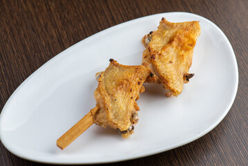 A plate of two chicken wings on a stick.