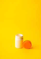 Vitamins soft capsules with pills bottle on a yellow background. Fingers holding herbal pill, closeup. Concept of health care,vitamins supplements, treatment of diseases. 