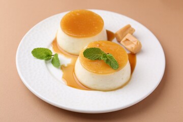 Tasty puddings with caramel sauce served on light brown background, closeup
