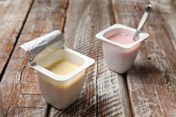 Delicious yogurts in plastic cups on wooden table, closeup
