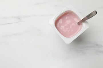 Delicious yogurt in plastic cup with spoon on white marble table, top view. Space for text