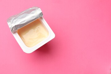 Delicious yogurt in plastic cup on pink background, top view. Space for text