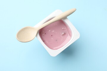 Delicious yogurt in plastic cup with spoon on light blue background, top view