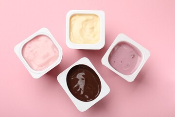 Delicious yogurts in plastic cups on pink background, flat lay