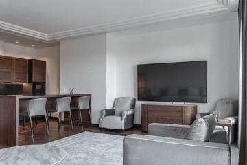 modern living room and kitchen design with matching furniture theme set. large TV, grey armchairs, wooden kitchen table and chairs. Wooden kitchen. Grey carpet, white walls, ceiling. Elegant interiors