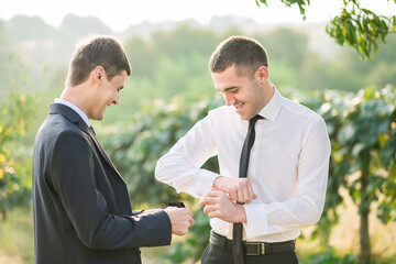 Two men are standing in a field, one of them is wearing a tie. They are smiling at each other