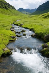 A stream of water flows through a grassy valley. The water is clear and the grass is lush and green. The scene is peaceful and serene