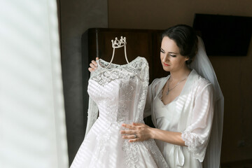 A bride is holding a dress up to her face. The dress is white and has a crown on it