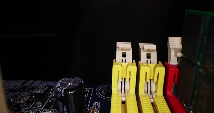 Slow motion of motherboard components - memory slots, ddr dimm memory, processor, sata, battery, capacitors, jumpers, chips, PCI on a black background close-up. Red, yellow, blue, orange connectors.