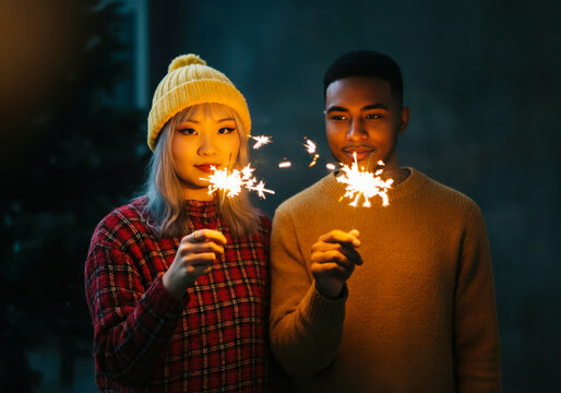 Young asian female and african male holding sparklers outdoors at night