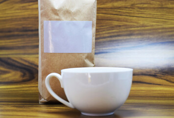 Empaque de café en blanco y taza de porcelana blanca, sobre una mesa de madera, espacio para texto al lado derecho.
