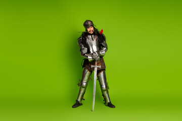Medieval knight in steel armor posing with a sword on a green background