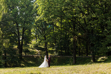 A bride and groom stand in a lush green field, surrounded by trees. Scene is serene and romantic, as the couple enjoys their special day in a beautiful outdoor setting