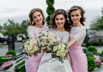 Three women are holding bouquets of flowers and posing for a picture. Scene is joyful and celebratory, as the women are likely attending a wedding or other special event