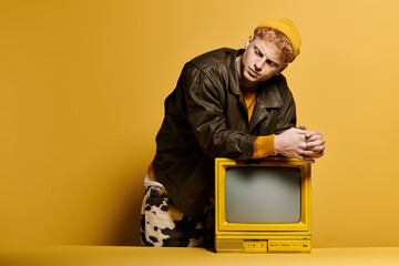 Stylish young man showcases trendy winter fashion while leaning on a vintage television.