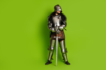 Portrait of a medieval knight in shiny armor holding his sword on a bright green background