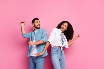 Fototapeta premium Cheerful young couple in casual outfits dancing against pink background, expressing joy and happiness