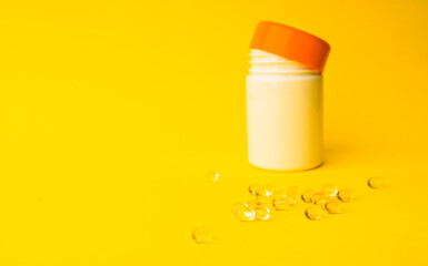 Vitamins soft capsules with pills bottle on a yellow background. Fingers holding herbal pill, closeup. Concept of health care,vitamins supplements, treatment of diseases. 