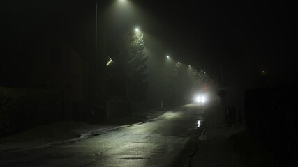 Lone car driving on a misty street under glowing streetlights.
