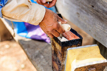 Farmer's hands placing organic fuel into instrument to add smoke to artisanal honeycombs.