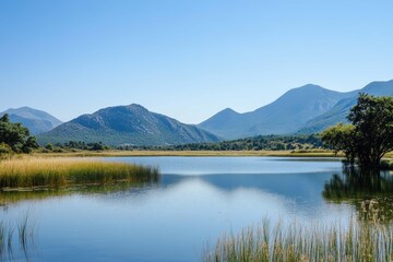 Serene lake surrounded by mountains and grassy landscapes under a clear blue sky in the early afternoon