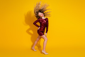 Stylish woman in a sequined red dress posing energetically against a vibrant yellow background, showcasing glamour and holiday cheer
