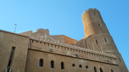 Fort Al-Jalali in Muscat, Oman, A stunning view of a historic fort with a prominent cylindrical tower, featuring traditional architecture and a flag against a clear blue sky.