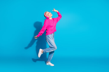 Obraz premium Joyful young woman in trendy pink sweater enjoying music, dancing with headphones against vibrant blue background