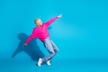 Young woman with short blonde hair strikes a playful pose against a vibrant blue background