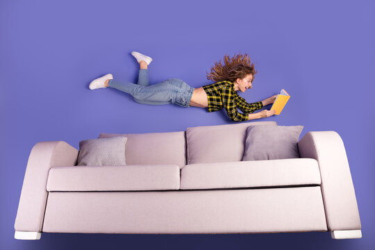 Young woman reading a book while seemingly floating above a sofa against a vibrant purple background.