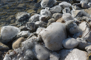 large stones by the edge of the lake covered in a thick coat of ice