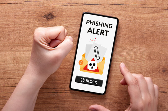 Overhead shot of a woman's hands reacting with frustration to a phishing alert on her smartphone, placed on a wooden surface. Online scam warnings concept.
