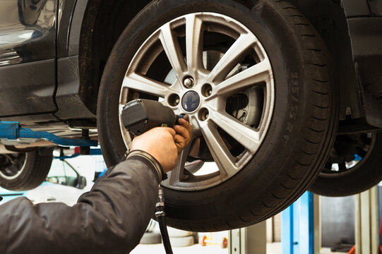 Mechanic changing car wheel using impact wrench in garage