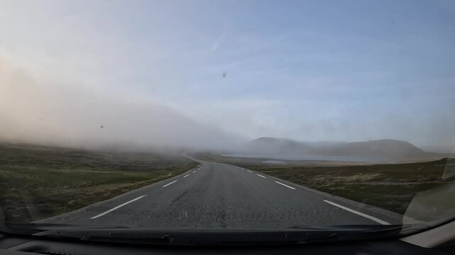 Driving through the tundra in northern Norway on E69 road. Surrounded by rocks and low grass. Foggy atmosphere creates a mysterious and serene landscape.