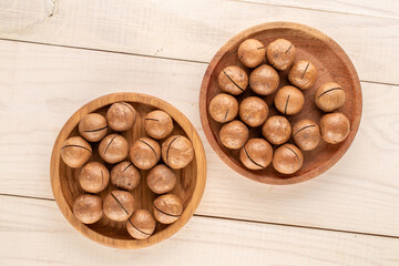 Macadamia nuts in shell with wooden plate on wooden table, top view.