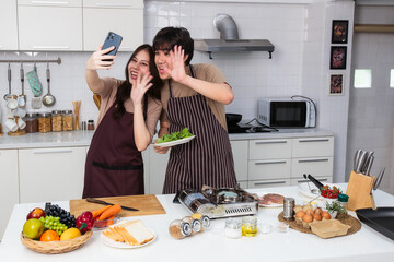 Lovely young Asian couple take a selfie photo while prepare ingredient for cooking together in home kitchen