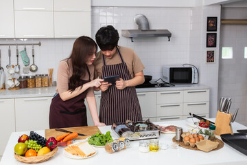 Loving young Asian couple prepare ingredient for cooking together by using instruction from tablet in home kitchen