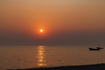 Sunset at Pattaya beach, Thailand, with fisherman ships and sun reflection on sea surface