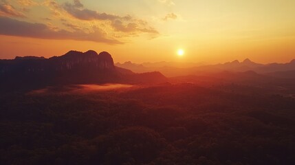 Aerial view of vibrant sunset over tropical forest highlighting ridged mountains and mist-covered landscape in the background