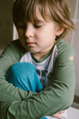 Little boy toddler is sitting alone on the floor and hugging his knees after suffering an act of bullying. 