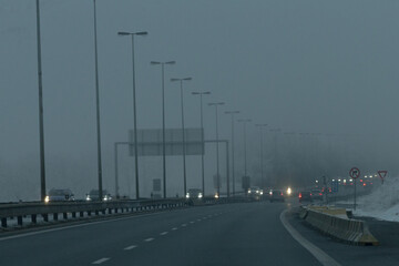 A long highway shrouded in foggy weather conditions, where streetlights cast a warm glow, illuminating the road ahead with limited visibility