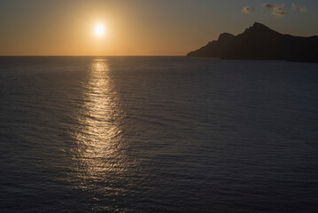 Sol reflejándose en el mar al atardecer junto a litoral montañoso