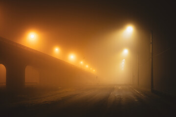 Moody orange street lights illuminating empty city road on a foggy winter night. No cars, no people