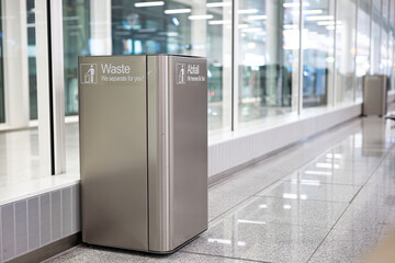Large, square, metal garbage bin or can inside international airport terminal lobby, no people