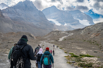 Line of tourist hikers heading up to the Athabasca Glacier in Jasper National Park with cloudy sky